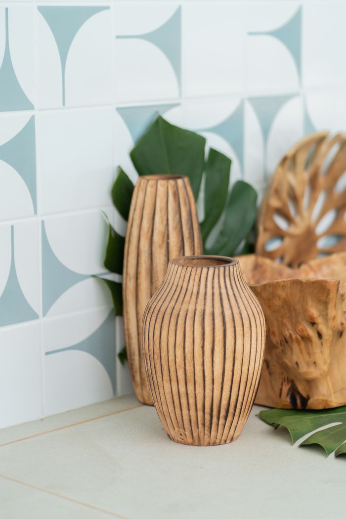Stylish carved wooden vases with leaf decor against geometric tiled wall.