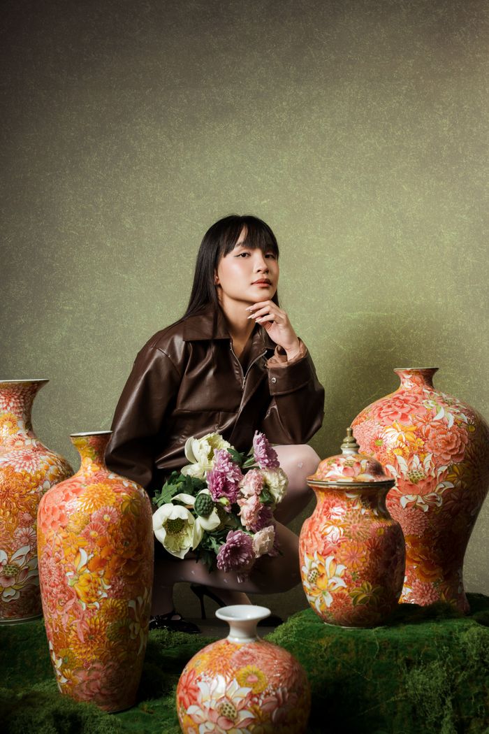 A woman poses among ornate vases, showcasing art and elegance indoors.