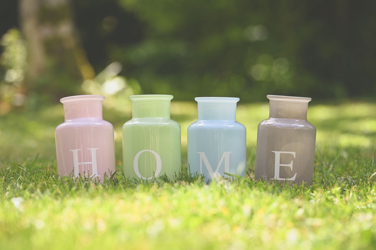 Pastel-colored vases spelling 'HOME' on green grass in bright outdoor setting.